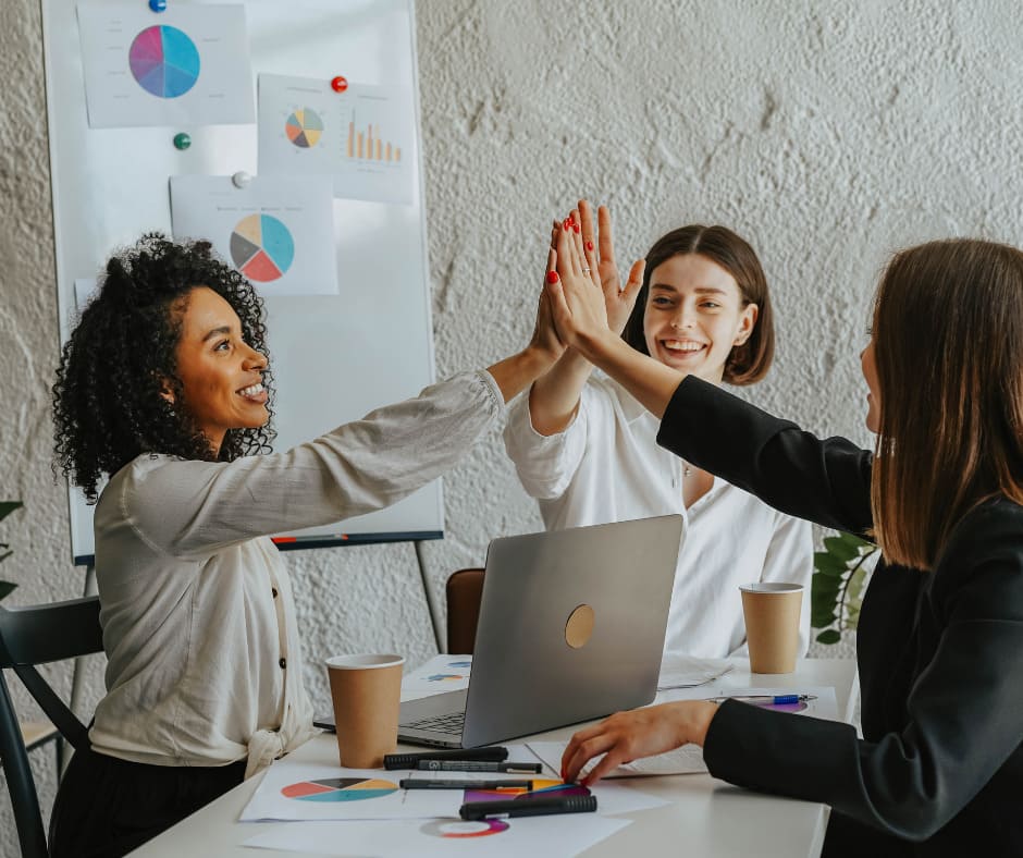 three women at a table giving each other high fives
