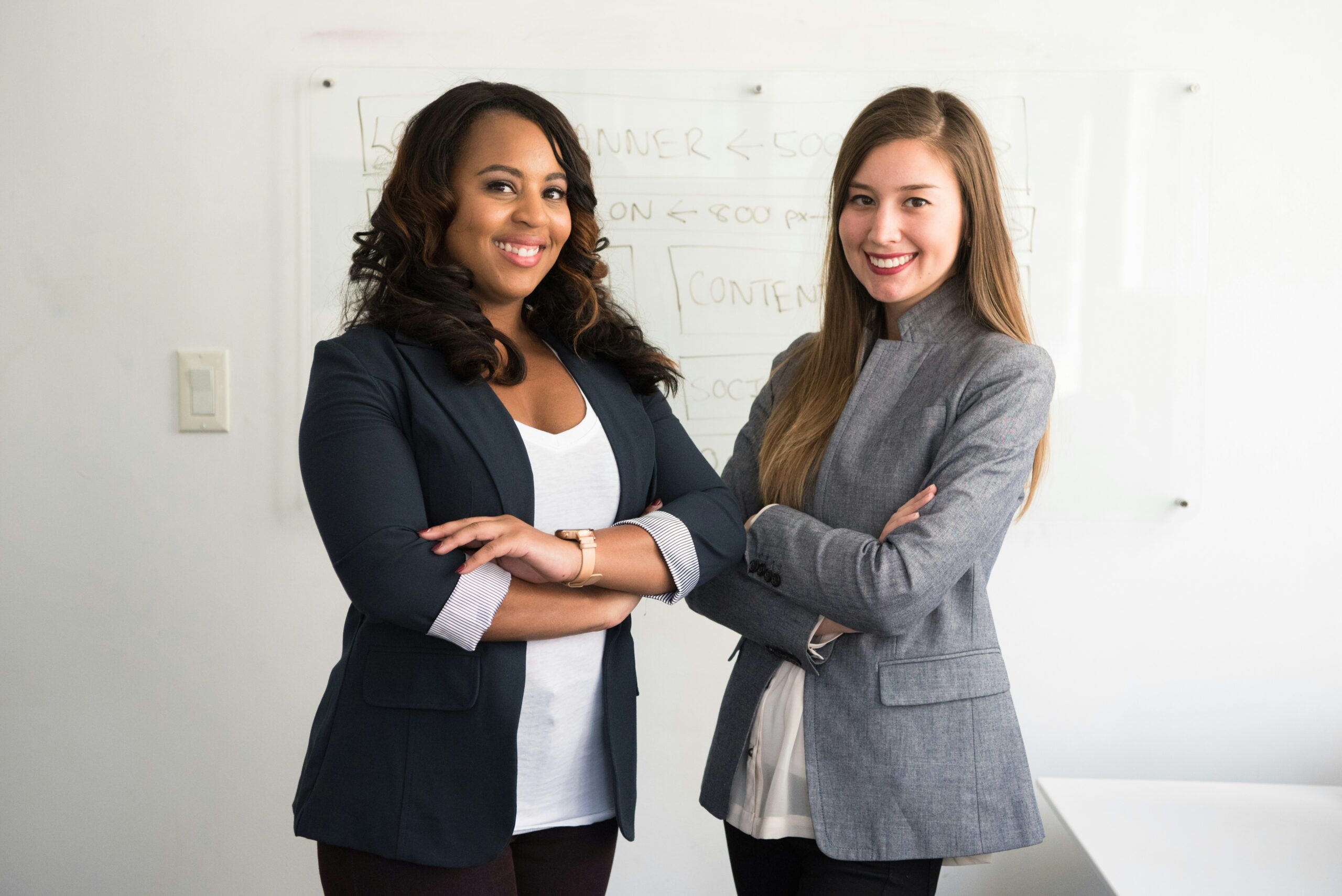 Two women with their arms crossed and smiling looking for women leadership mentorship platforms.