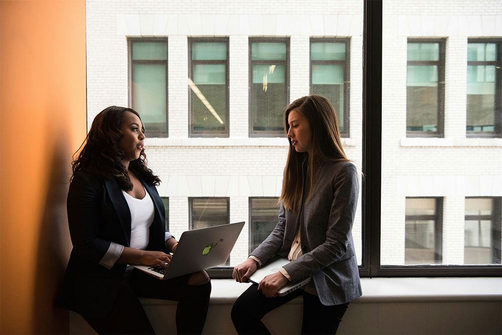 Two business women in a private conversation by a window during women in business conferences.